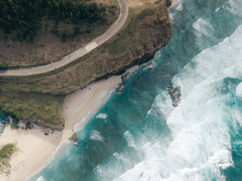 Aerial view of a winding coastal road, cliffs, beach, and turquoise ocean waves breaking. Ly Son island, Vietnam