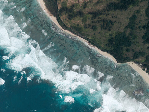 Aerial view of waves crashing on a sandy coastline with lush green vegetation nearby. Ly Son island, Vietnam