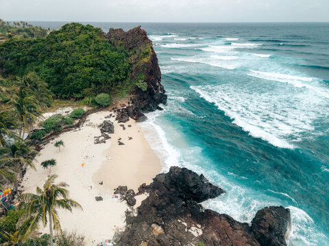 Aerial view of a tropical beach with lush greenery and rocky cliffs by the turquoise ocean. Ly Son island, Vietnam