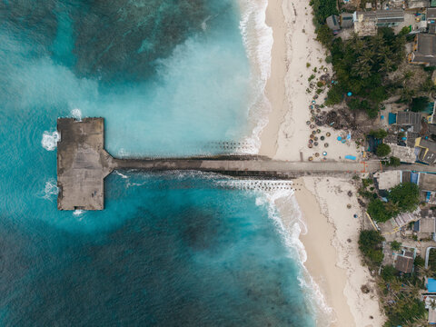 Aerial view of pier extending into turquoise ocean, sandy beach flanked by lush greenery. Ly Son island, Vietnam