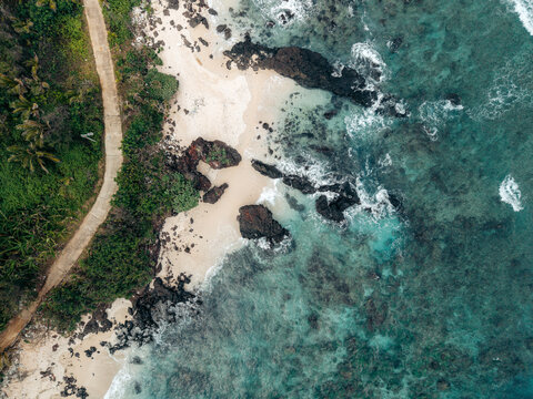 Aerial view of a rocky coastline with clear turquoise waters and lush greenery along a sandy beach. Ly Son island, Vietnam