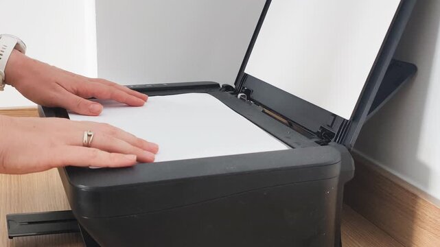 Concept of modern document scanning for corporate business routine. Hand places a white A4 paper on a glass surface during document scanning process to copy and archive important information.