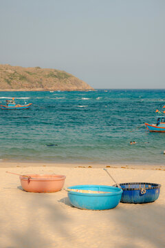 Three colorful round tubs on a sandy beach with blue ocean and boats in the background.
