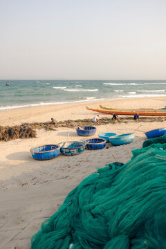 Sandy beach with fishing nets, round boats, and gentle waves on a sunny day.