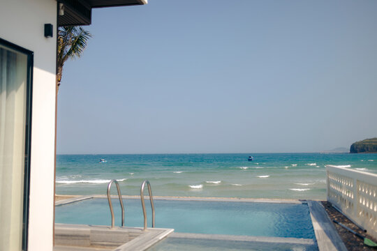 Infinity pool overlooking a bright blue ocean under a clear sky, next to a modern white building.