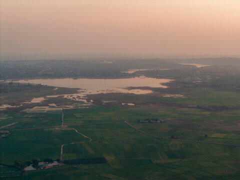 Aerial view of a vast landscape with green fields, a large lake, and a hazy orange sky.
