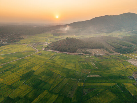 Aerial view of lush green fields at sunset with a mountain in the background, emitting a warm glow.