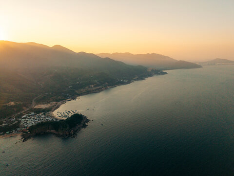Aerial view of a serene coastal landscape at sunset with mountains and sea.