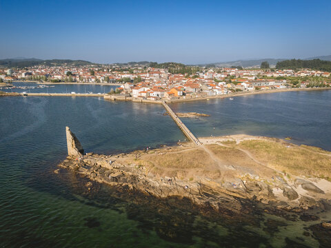 Aerial view of a coastal village with a stone bridge leading to a small rocky island.