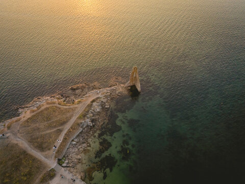 Aerial view of a rocky coastal outcrop at sunset with calm sea and warm colors.