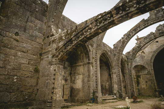 Ancient stone arches of a weathered, historic ruin under a cloudy sky.
