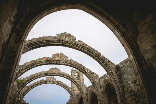 Stone arches of ancient ruins with intricate carvings under a cloudy sky.