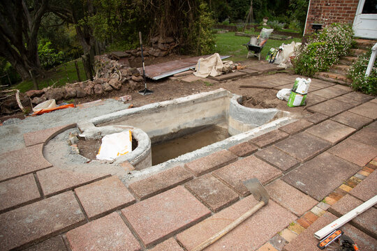 Backyard construction site with an unfinished concrete pond surrounded by bricks and tools. Auckland, New Zealand