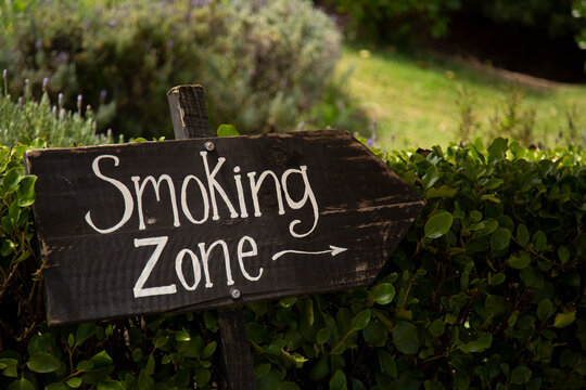Wooden sign with Smoking Zone written on it, set against lush greenery.