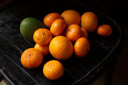 A variety of oranges and an avocado on a dark wooden surface.