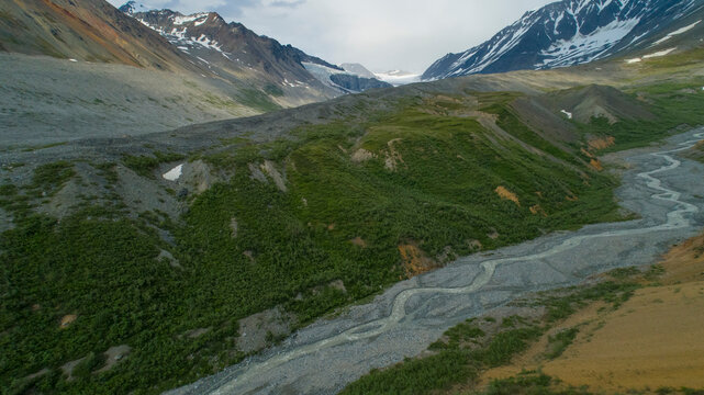 Aerial view of a winding river through a lush green valley surrounded by snow-capped mountains. Isabel Pass, Alaska, USA