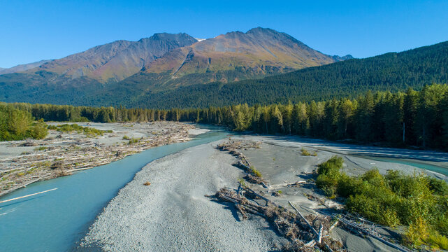 A winding river flows through a forest with mountains in the background under a clear blue sky. Moose Pass, Alaska, USA