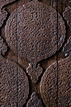 Ornate carved wooden door detail from Muhammad Amin Khan Madrasah in Khiva. Carved wood texture, pattern, background. Intricate floral arabesque medallion pattern on aged wood panels.