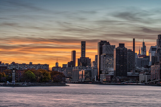 A vibrant city skyline at sunset with reflections on the calm water. New York, USA