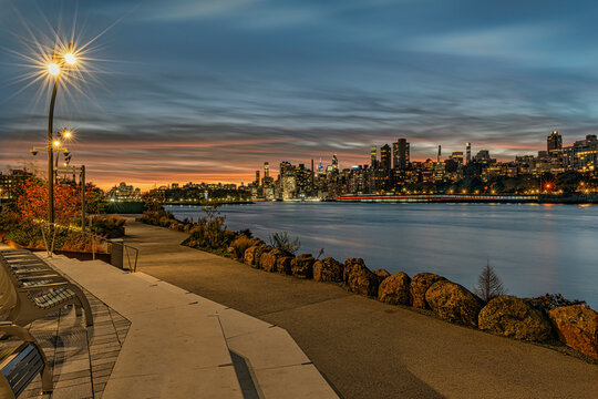 Evening cityscape with illuminated skyline and serene river view under a vibrant sunset sky. New York, USA