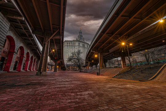 Illuminated bridge and archways in urban setting with a building under dramatic cloudy sky. New York, USA