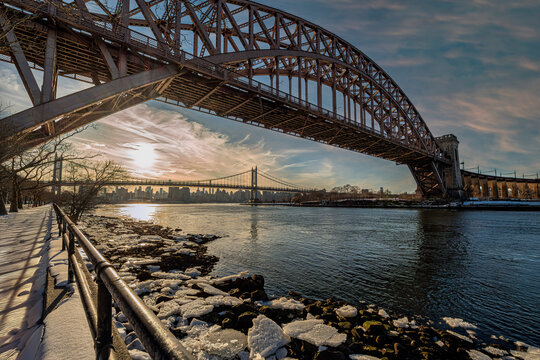 Sunlit view of a steel arch bridge over a river with a city skyline in the distance. New York, USA