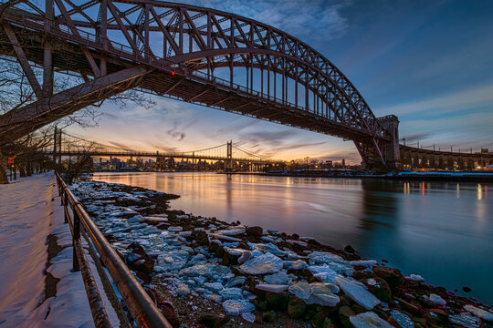 Stunning sunset view of steel bridge arching over a serene river with icy banks in winter. New York, USA