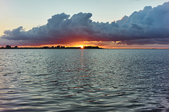 Dramatic sunset over calm ocean waters with vibrant, colorful clouds in the sky.