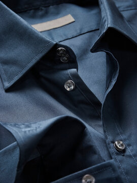 Close-up of a blue silk shirt with shiny buttons on a smooth fabric surface.
