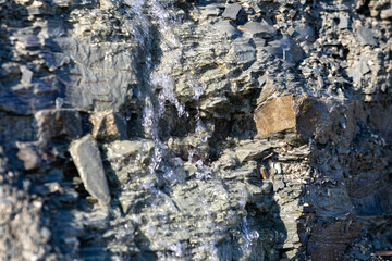 Fototapeta premium Quebec, Canada, 11 June 2026 : Water cascades down a textured rock face with visible layers and small stones