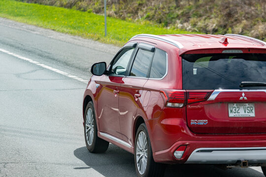 Gaspesie, Canada, 30 May 2026 : Red Mitsubishi Outlander PHEV SUV drives on an asphalt road with green grass on the shoulder