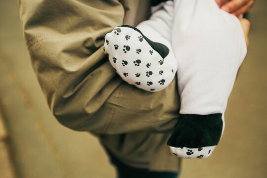 Close up of a baby wearing cute white footie pajamas with black animal paw prints on the soles being held in a parent's arms.