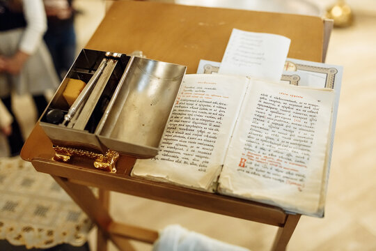 Close up of an open silver holy oil box with a brush and sponge next to an open liturgical book on a wooden stand in a church.