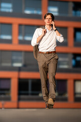 Fototapeta premium Young businessman talking on smartphone walking outside office