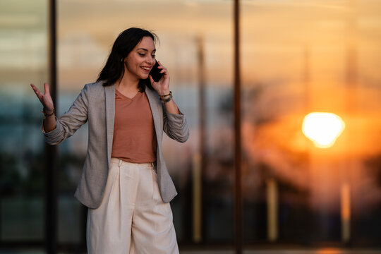 Businesswoman talking cheerfully on phone during golden hour sunset