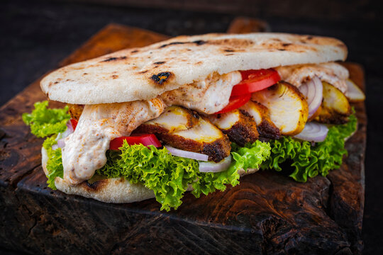 Classic fingerfood fastfood snack -  traditional panino imbottito - Italian flat bread sandwich with roasted chicken, vegetable salad and dressing sauce served as close-up on a wooden board