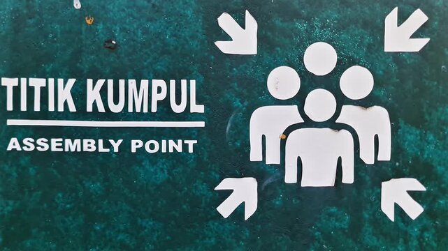 Sidoarjo, Indonesia - 18 June, 2026: Weathered Green Assembly Point and Titik Kumpul Emergency Evacuation Sign on Peeling Metal Board