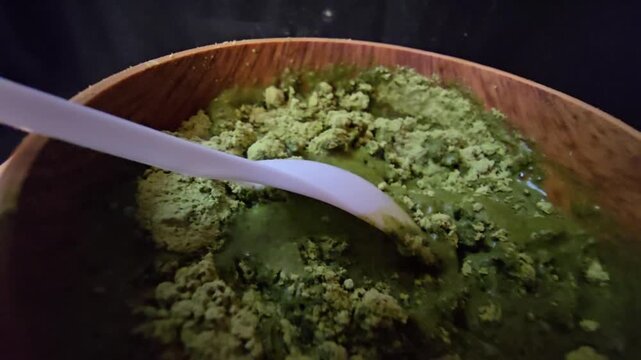 Close-up of mixing Sidr (Ziziphus spina-christi ) herbal powder with water in a wooden bowl, demonstrating the texture of a natural skincare preparation.
