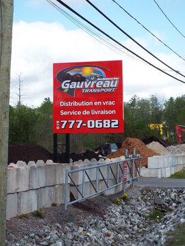 Chelsea,Quebec, Canada &ndash; May 14, 2026: A vibrant red roadside sign advertises "Gauvreau Transport", specializing in bulk distribution and delivery services with contact information on Quebec Rte.