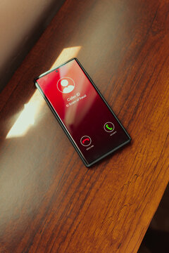 Scam call alert on smartphone screen with red caller ID warning on wooden desk. Scam awareness, fraud prevention, and digital security.