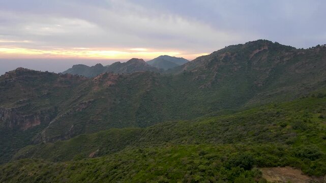 Aerial view of the lush green Margalla Hills at sunset with rolling ridges and soft evening light over the landscape in Islamabad, Punjab, Pakistan.