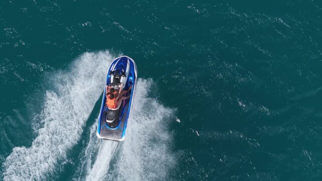 Direct top-down aerial view tracking a mother and daughter riding a blue jet ski, carving through deep turquoise waters at Beau Vallon, Seychelles with exploding white wakes.