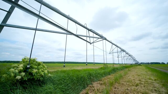 Large industrial agricultural irrigation system in a green farm field next to a dirt road under a cloudy sky.