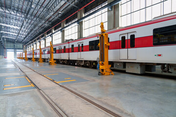 Obraz premium Red and white subway trains are expertly raised on hydraulic jacks inside vast modern train maintenance hall with large windows, featuring advanced repair equipment for urban transit systems.