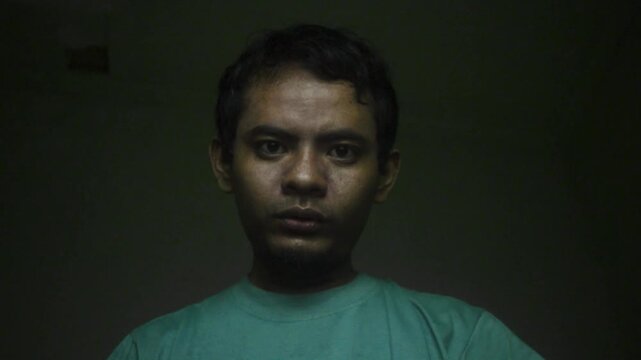Portrait Of A Young Asian Man Making Aggressive Threatening Gestures Against A Dark Green Background