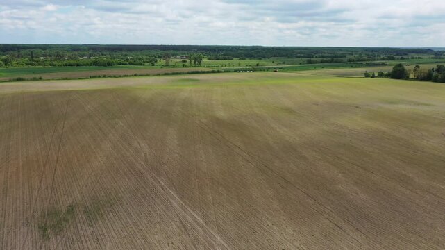 Aerial top view of a green agricultural tractor spraying chemicals, fertilizer, or pesticides on a large farming field with visible rows.