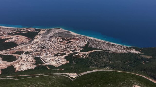 Aerial view of coastal construction sites and residential rooftops along the turquoise waters of the Ionian Sea in Dhermi, Vlore County, Albania.
