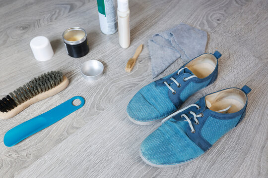 Blue nubuck leather shoes care kit with brush wax polish cream on grey floor. Premium footwear maintenance routine for high quality material protection and long lasting shoe durability. Clean suede