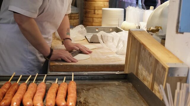 chef rolls soft dough on wooden board in busy asian street food stall. preparing fresh dough requires skill and traditional manual techniques. chef uses rolling pin to shape dough into thin wrapper