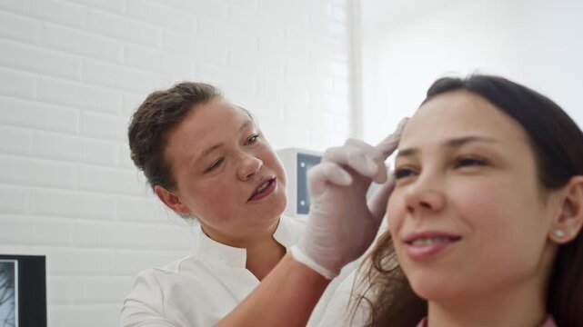 Caucasian female trichologist examining hair of smiling female patient in clinic. Clip perfect for hair loss treatment ads and dermatology clinic marketing
